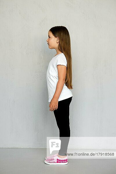 Cute young child with long hair in white t-shirt and black sweatpants standing in profile