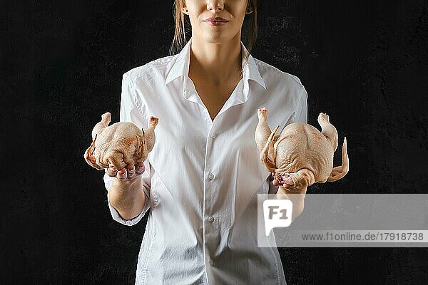 Unerkennbare Frau hält rohes Huhn in einer Hand und ein kleines Küken in der anderen