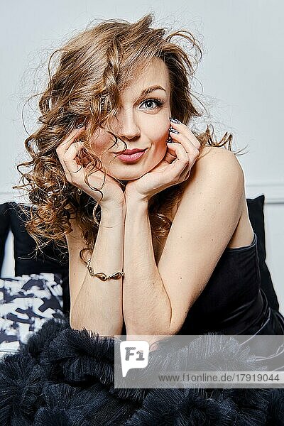 Portrait of beautiful and elegant young woman with natural makeup and curly hair propping her chin with her hands