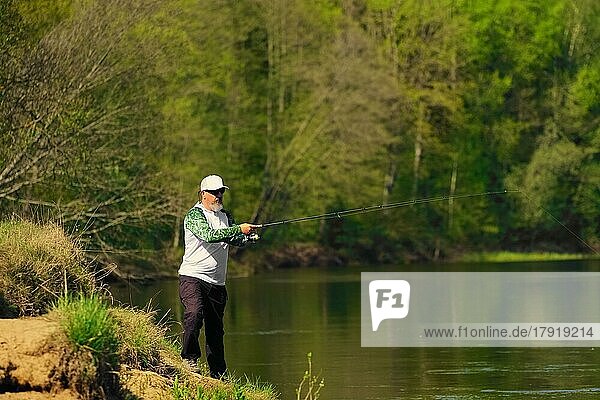 Mann fischt mit Spinning am Flussufer  wirft Köder. Wochenendaktivität im Freien. Foto mit geringer Schärfentiefe bei weit geöffneter Blende aufgenommen