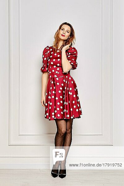 Portrait of young woman in dotted satin dress and polka dot tights near the wall