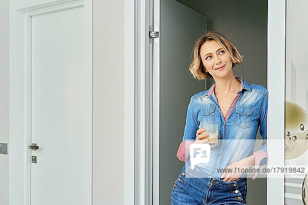Junge Frau steht in der Tür des Schlafzimmers mit einem Glas Cappuccino in der Hand
