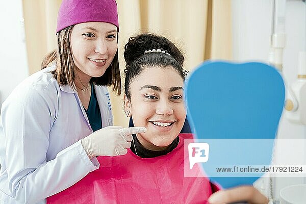 Zahnarzt mit zufriedenem Patienten  der in den Spiegel lächelt  zufriedener Patient in der Zahnklinik  der in den Spiegel schaut  weiblicher Patient  der die Zähne nach der Zahnbehandlung in der Zahnklinik kontrolliert