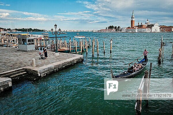 VENEDIG  ITALIEN  27. JUNI 2018: Gondoliere mit Touristen in einer Gondel in der Lagune von Venedig am Markusplatz mit der Kirche San Giorgio di Maggiore im Hintergrund in Venedig  Italien  Europa