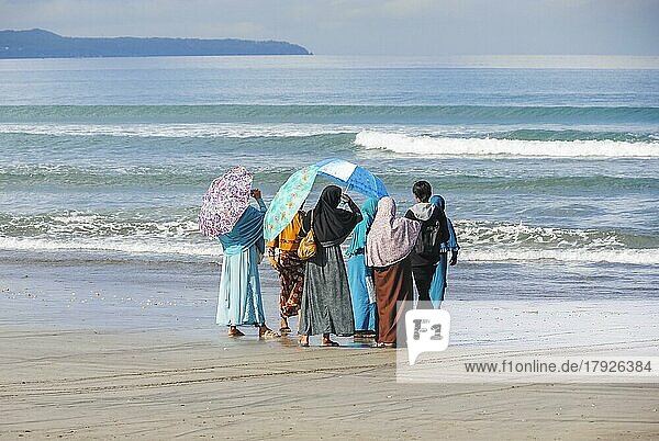 Muslimische Frauen und ein junger Mann schauen am Strand von Bali  Indonesien  ins Meer  Asien