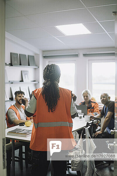 Rear view of carpenter discussing with colleagues in warehouse office during meeting