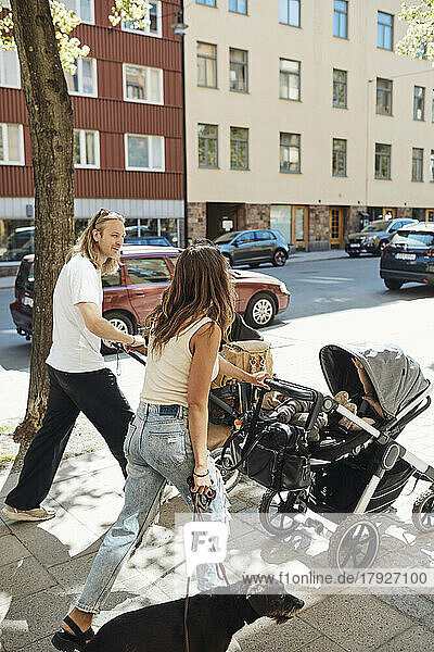 Man and woman talking while pushing strollers with children on sidewalk