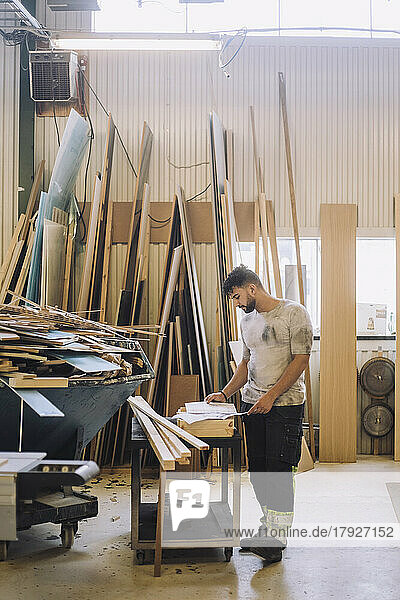 Männlicher Schreiner in voller Länge  der an einer Werkbank in einer Werkstatt einen Bauplan liest