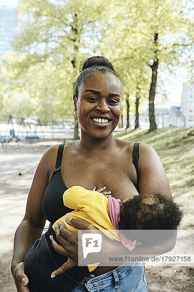 Porträt einer glücklichen Frau  die ihre Tochter im Park stillt