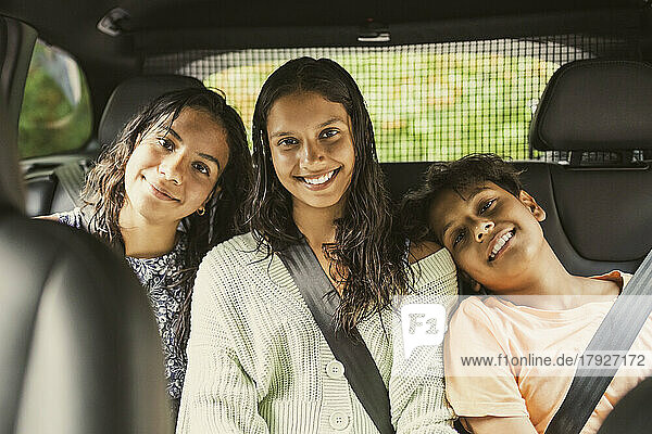 Porträt eines lächelnden Geschwisterpaares  das angeschnallt auf dem Rücksitz eines Autos sitzt
