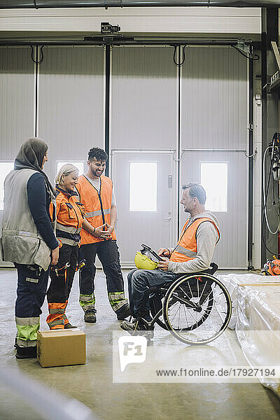 Zimmermann im Rollstuhl sitzend  der mit einem männlichen und einem weiblichen Kollegen im Lagerhaus diskutiert