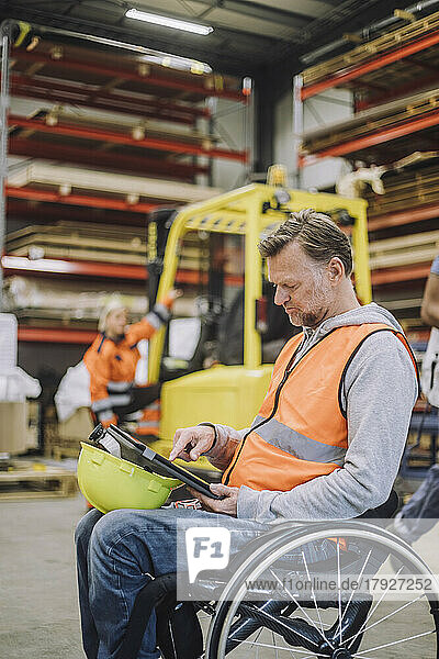 Male carpenter with disability using digital tablet sitting on wheelchair in warehouse
