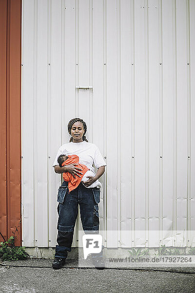 Ganzkörperporträt einer Bauarbeiterin mit ihrer kleinen Tochter vor einer Metallwand