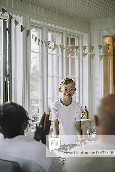 Smiling boy serving food during dinner party at home