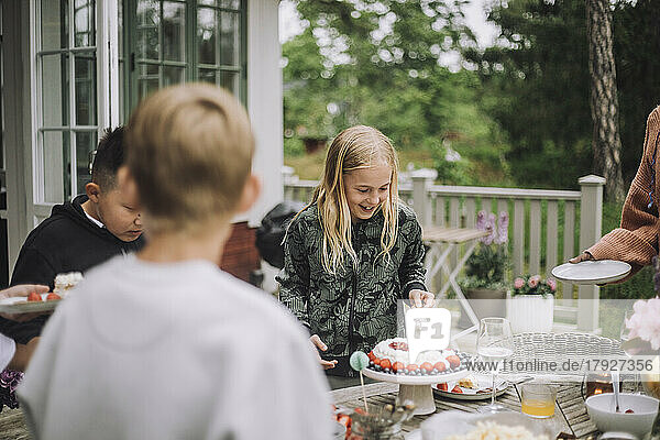 Mädchen schneidet Geburtstagskuchen an  während sie in der Nähe des Tisches steht