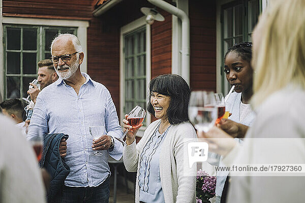 Glückliche Frau mit Weinglas in der Hand und Familie bei geselligem Beisammensein