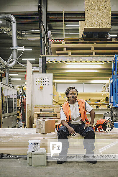 Portrait of female blue-collar worker sitting by hardhat in warehouse