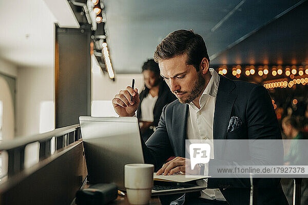 Junger Geschäftsmann liest Tagebuch  während er mit Laptop im Hotel sitzt