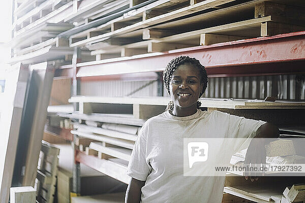 Porträt eines glücklichen Zimmermanns  der vor einem Palettenstapel in einem Lagerhaus steht