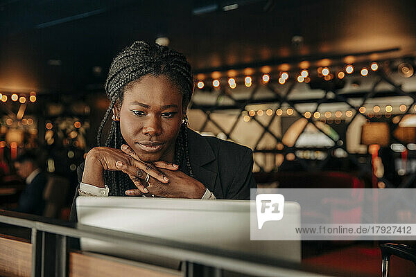 Junge Geschäftsfrau mit verschränkten Händen vor einem Laptop in einer Hotelhalle