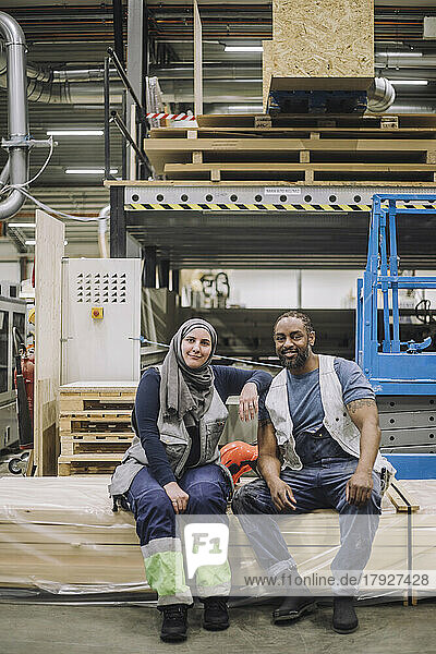 Full length portrait of female worker sitting with colleague in warehouse
