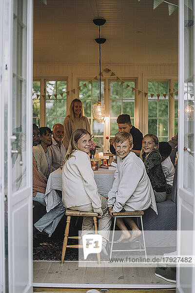 Junge und Mädchen schauen über die Schulter  während sie auf einem Hocker am Esstisch mit ihrer Familie sitzen