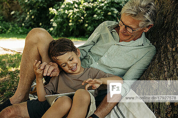 Junge benutzt digitales Tablet  während er mit seinem Großvater im Park sitzt