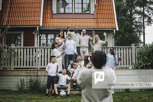 Frau fotografiert fröhliche Mehrgenerationenfamilie auf der Veranda vor dem Haus