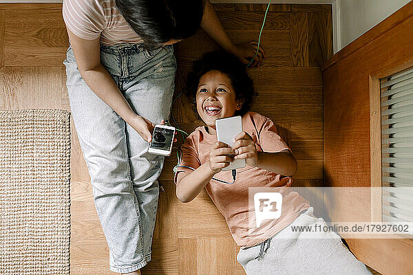 Directly above shot of happy siblings using smart phones on hardwood floor at home
