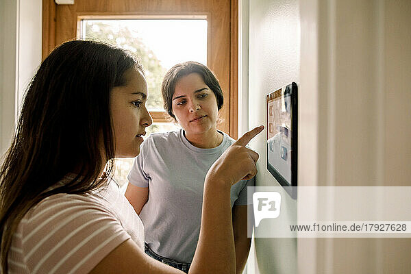 Mutter bringt ihrer Tochter bei  wie man die Hausautomatisierung auf einem digitalen Tablet nutzt  das zu Hause an der Wand montiert ist