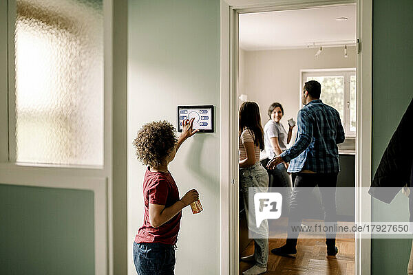 Side view of boy using smart home app on digital tablet while family standing in kitchen