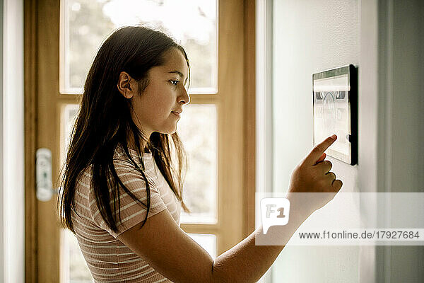 Seitenansicht eines Mädchens  das die Hausautomatisierung über einen an der Wand montierten Tablet-PC nutzt