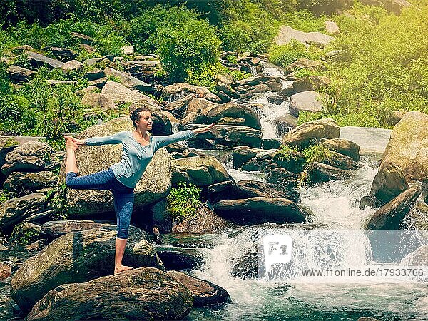 Yoga im Freien  Frau macht Yoga-Asana Natarajasana  Herr des Tanzes Gleichgewichtspose im Freien am Wasserfall im Himalaya. Vintage Retro-Effekt gefiltert Hipster-Stil Bild