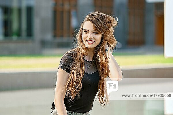Positive und glückliche junge Frau mit langen lockigen Haaren im Freien