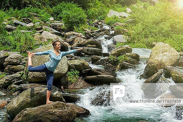 Yoga im Freien  Frau macht Yoga-Asana Natarajasana  Herr des Tanzes Gleichgewichtspose im Freien an einem Wasserfall im Himalaya
