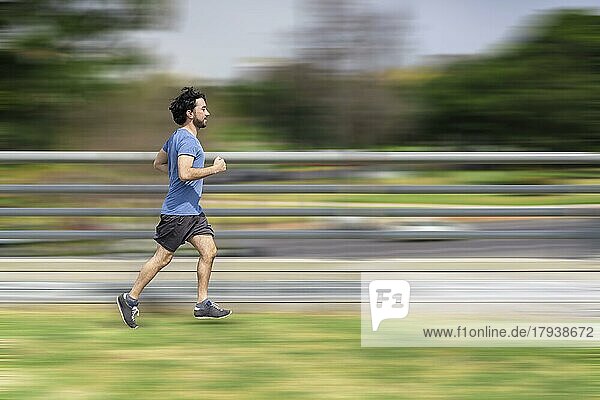 Porträt von gut aussehend attraktiv reifen bärtigen sportlichen lateinischen Mann Mann 40s in lässigen blauen T-Shirt läuft in einem Park. Geschwindigkeit Konzept. Bewegung Unschärfe Hintergrund