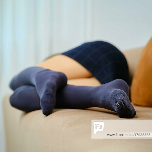 Frauenbeine in kariertem Rock und Overknee-Socken auf der Couch zu Hause (selektiver Fokus mit geringer Schärfentiefe)