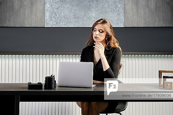 Junge Frau  die im Büro hinter dem Schreibtisch sitzend auf die Verbindung eines Online-Anrufs wartet