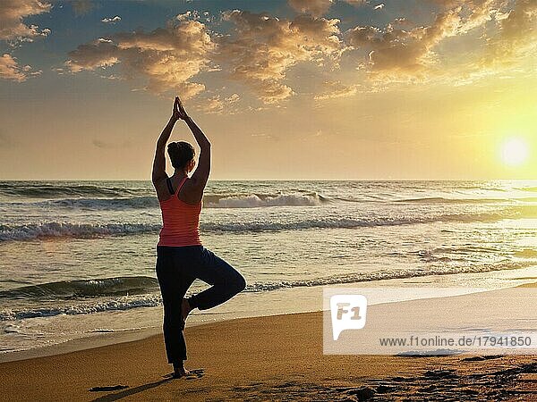 Yoga im Freien  sportlich fitte Frau macht Hatha Yoga Asana Vrikshasana tre Pose am tropischen Strand bei Sonnenuntergang