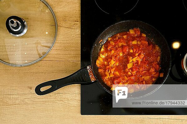 Draufsicht auf eine Bratpfanne mit Tomatensauce auf einem modernen Elektroherd  der Glasdeckel liegt daneben