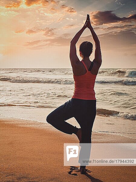 Vintage Retro-Effekt gefiltert Hipster-Stil Bild von Yoga im Freien  sportlich fit Frau tun Hatha-Yoga-Asana Vrikshasana tre Pose am tropischen Strand bei Sonnenuntergang