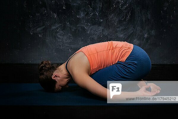Schöne sportliche fit Yogini Frau Praktiken Yoga Asana Balasana (Child's Pose)  Ruhehaltung oder Gegen Asana für viele Asanas auf dunklem Hintergrund