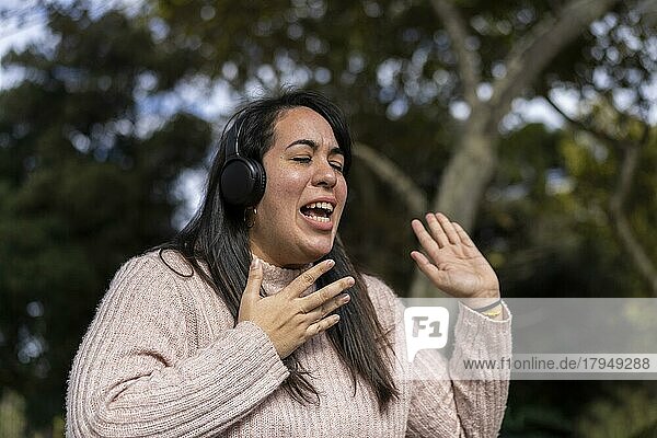 Junge lateinamerikanische Frau  die im Freien mit Kopfhörern Musik hört. Ausdruck von Glück  gewinnende Einstellung. Textfreiraum