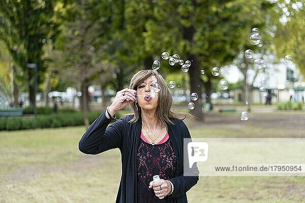 Reife Transfrau beim Blasen von Seifenblasen in einem Park
