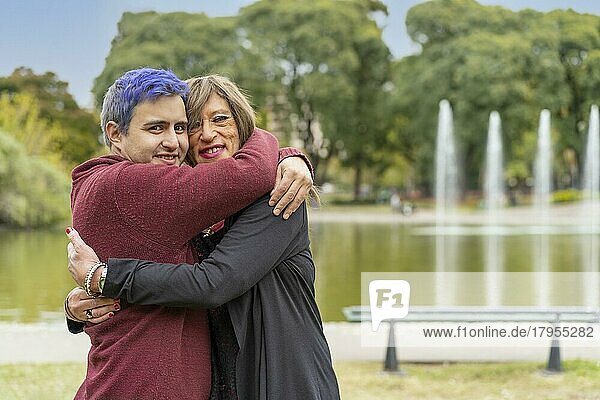 Fröhliches queeres Paar  das sich in einem Park umarmt und in die Kamera schaut