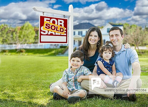 Junge Familie mit Kindern vor maßgeschneidertem Haus und zum Verkauf stehendem Immobilienschild