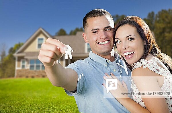 Gemischtrassiges  aufgeregtes Militärpaar vor seinem neuen Haus  das seine Hausschlüssel vorzeigt