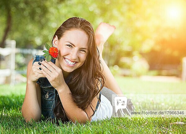 Attraktives gemischtrassiges Mädchen träumt im Gras liegend im Freien mit Blume