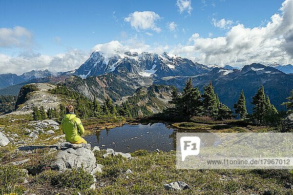 Hiker sitting on a rock  Small mountain lake on Tabletop Mountain  Mt. Shuksan with snow and glacier  Mt. Baker-Snoqualmie National Forest  Washington  USA  North America