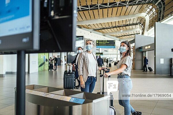 Zwei Reisende mit Schutzmasken diskutieren auf dem Flughafen von Faro mit einer Fluginformationstafel